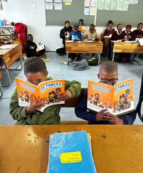Kinder lesen illustrierte FableReads-Bücher an ihren Tischen.