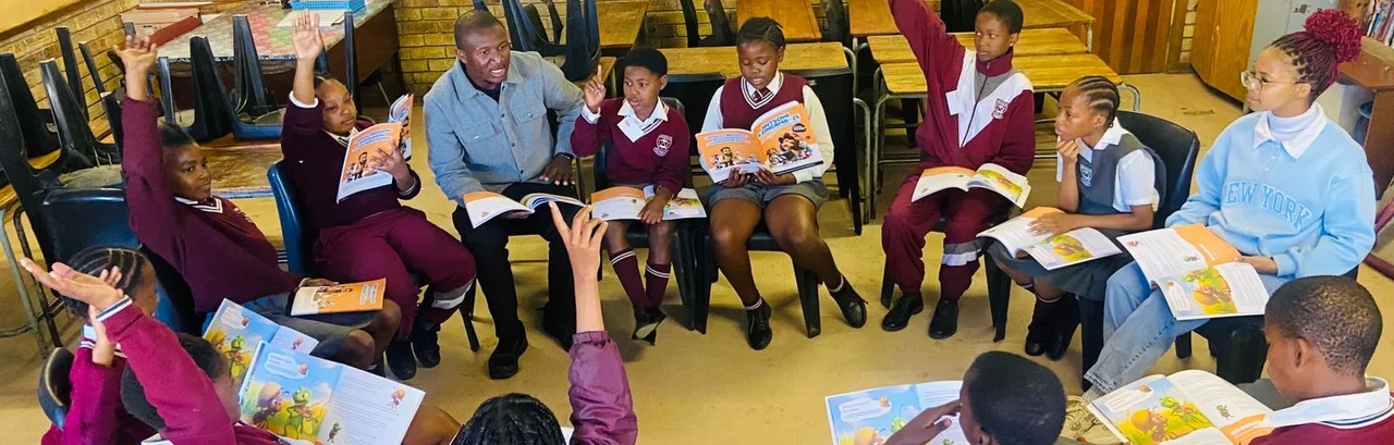 Learners holding FableReads books and raising their hands in a reading circle at John Masiza Primary.